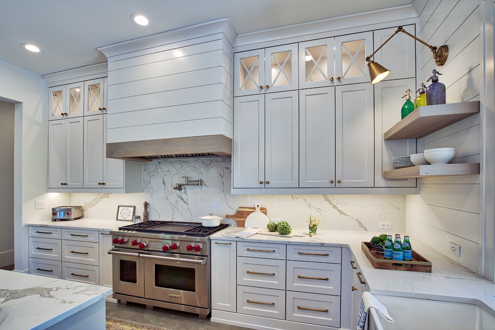 Photo of a large farmhouse u-shaped kitchen/diner in Atlanta with a belfast sink, shaker cabinets, white cabinets, engineered stone countertops, white splashback, stone slab splashback, stainless steel appliances, concrete flooring, an island, grey floors and white worktops.