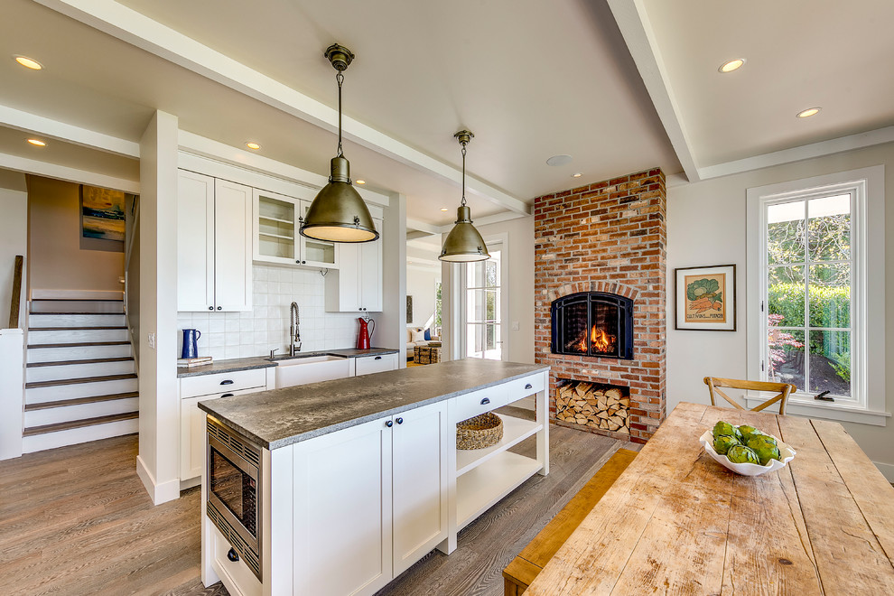 Large cottage l-shaped medium tone wood floor enclosed kitchen photo in Seattle with a farmhouse sink, shaker cabinets, white cabinets, soapstone countertops, white backsplash, ceramic backsplash, stainless steel appliances, an island and gray countertops