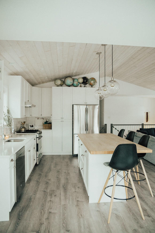 Bild på ett mellanstort skandinaviskt kök, med en undermonterad diskho, skåp i shakerstil, vita skåp, bänkskiva i kvarts, vitt stänkskydd, stänkskydd i tunnelbanekakel, rostfria vitvaror, vinylgolv och en köksö