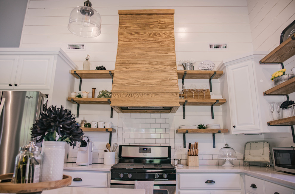 Inspiration for a mid-sized cottage l-shaped medium tone wood floor and brown floor kitchen remodel in Oklahoma City with a farmhouse sink, raised-panel cabinets, white cabinets, quartz countertops, white backsplash, subway tile backsplash, stainless steel appliances, an island and white countertops