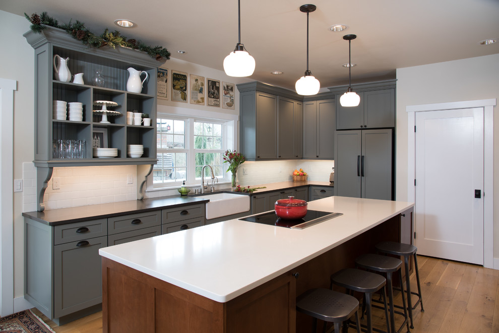 Foto på ett stort lantligt grå kök, med en rustik diskho, skåp i shakerstil, bänkskiva i kvarts, vitt stänkskydd, stänkskydd i keramik, rostfria vitvaror, en köksö, gröna skåp, mellanmörkt trägolv och brunt golv