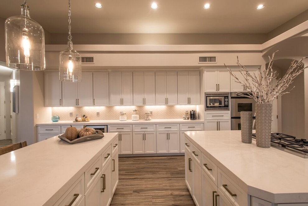 This is an example of an expansive classic l-shaped kitchen/diner in Phoenix with recessed-panel cabinets, white cabinets, composite countertops, beige splashback, ceramic splashback, stainless steel appliances, dark hardwood flooring, brown floors, a submerged sink and a breakfast bar.