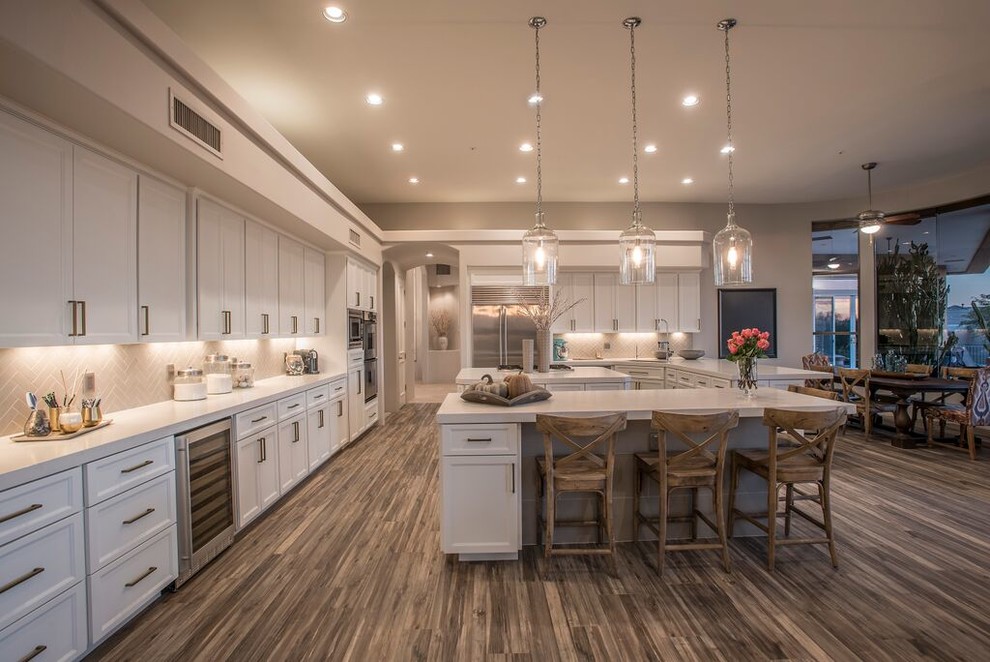 Example of a huge transitional l-shaped dark wood floor and brown floor eat-in kitchen design in Phoenix with an undermount sink, recessed-panel cabinets, white cabinets, solid surface countertops, beige backsplash, ceramic backsplash, stainless steel appliances and a peninsula
