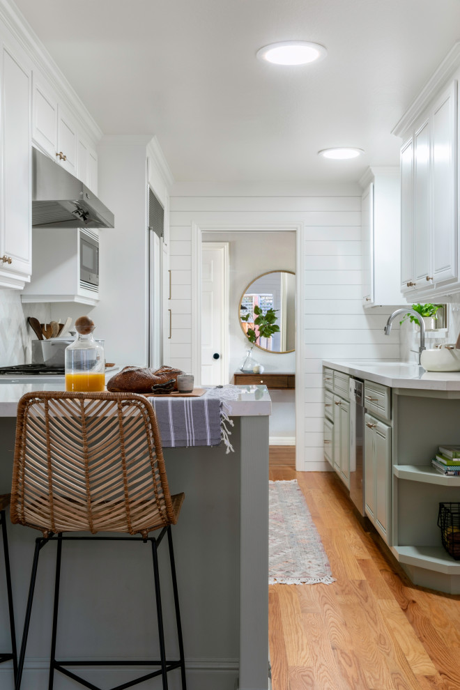 Small farmhouse galley light wood floor enclosed kitchen photo in San Francisco with a drop-in sink, raised-panel cabinets, green cabinets, quartz countertops, white backsplash, cement tile backsplash, stainless steel appliances, a peninsula and white countertops