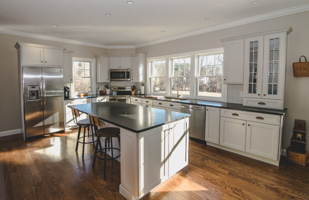 Inspiration for a large country l-shaped medium tone wood floor and brown floor open concept kitchen remodel in Boston with an undermount sink, shaker cabinets, beige cabinets, granite countertops, beige backsplash, wood backsplash, stainless steel appliances and an island