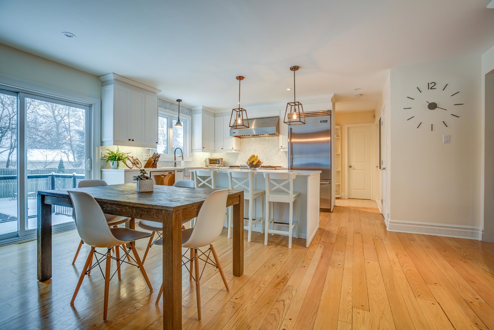 Eat-in kitchen - mid-sized transitional light wood floor eat-in kitchen idea in Montreal with a farmhouse sink, shaker cabinets, white cabinets, white backsplash, marble backsplash, stainless steel appliances, an island, quartz countertops and white countertops