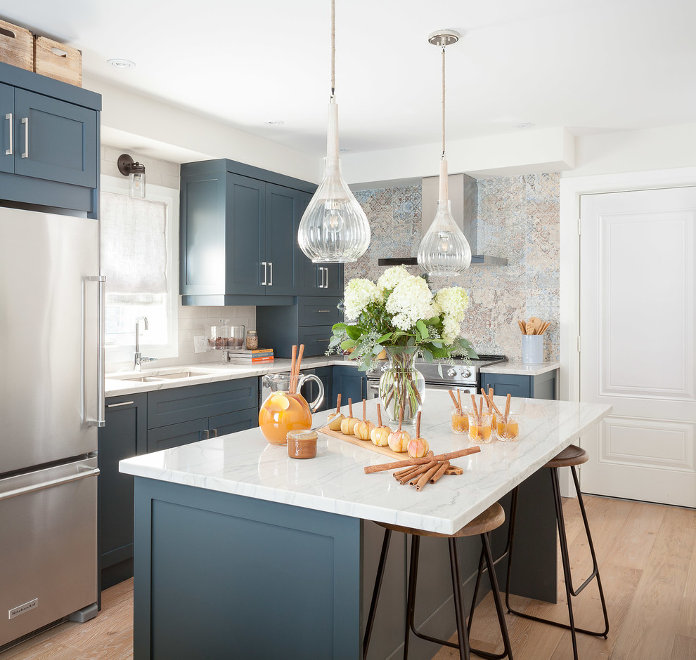 This is an example of a medium sized rural l-shaped enclosed kitchen in Toronto with shaker cabinets, blue cabinets, stainless steel appliances, an island, marble worktops, cement tile splashback and light hardwood flooring.