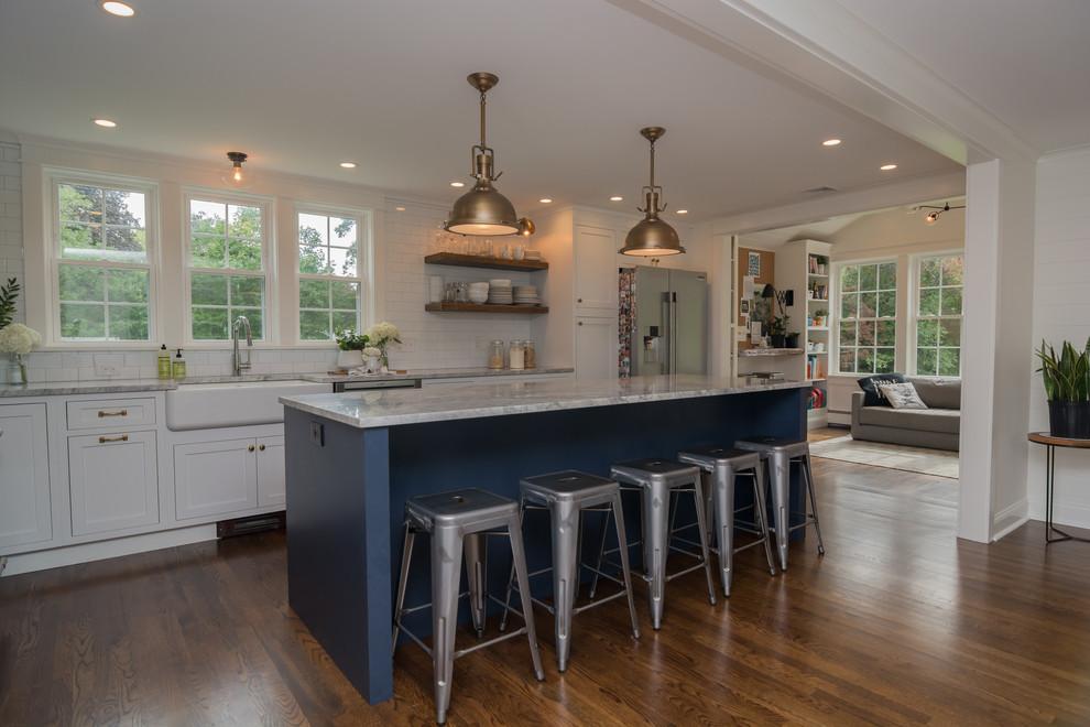 Inspiration for a mid-sized farmhouse l-shaped dark wood floor and brown floor eat-in kitchen remodel in Boston with a farmhouse sink, shaker cabinets, white cabinets, quartzite countertops, white backsplash, ceramic backsplash, stainless steel appliances, an island and gray countertops
