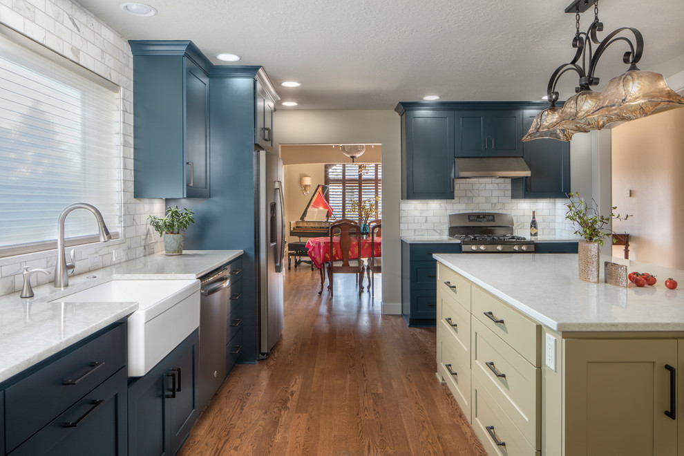 Eat-in kitchen - mid-sized country galley medium tone wood floor eat-in kitchen idea in Portland with a farmhouse sink, recessed-panel cabinets, blue cabinets, marble countertops, white backsplash, marble backsplash, stainless steel appliances, an island and white countertops