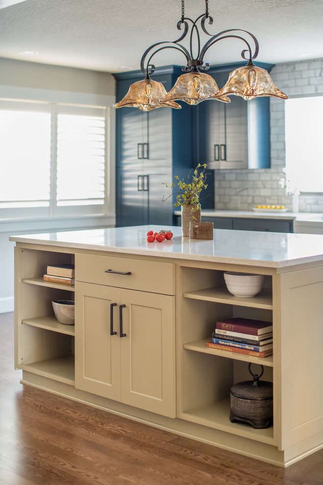 Lantlig inredning av ett mellanstort vit vitt kök, med en rustik diskho, luckor med infälld panel, blå skåp, marmorbänkskiva, vitt stänkskydd, stänkskydd i marmor, rostfria vitvaror, mellanmörkt trägolv och en köksö