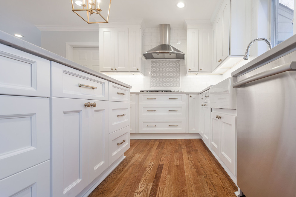 Design ideas for a large country l-shaped open plan kitchen in DC Metro with a belfast sink, shaker cabinets, white cabinets, engineered stone countertops, white splashback, ceramic splashback, stainless steel appliances, medium hardwood flooring, an island, brown floors and yellow worktops.