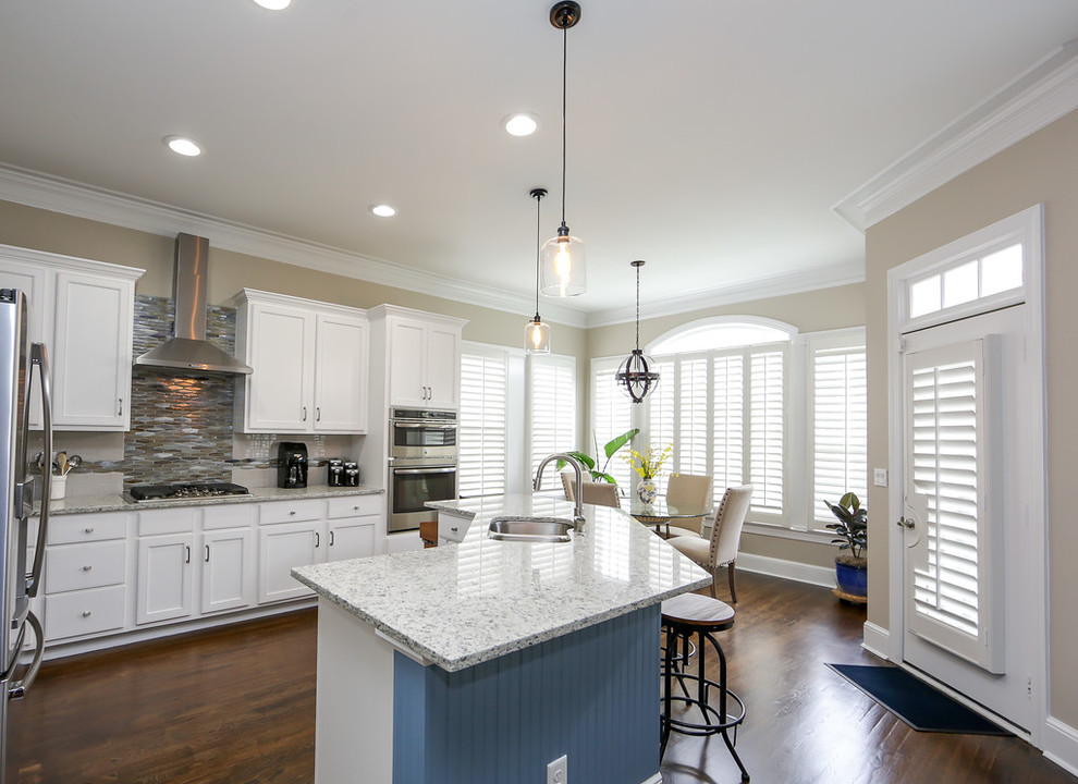 Mid-sized transitional l-shaped medium tone wood floor and brown floor open concept kitchen photo in Atlanta with an undermount sink, shaker cabinets, white cabinets, granite countertops, beige backsplash, glass sheet backsplash, stainless steel appliances and an island