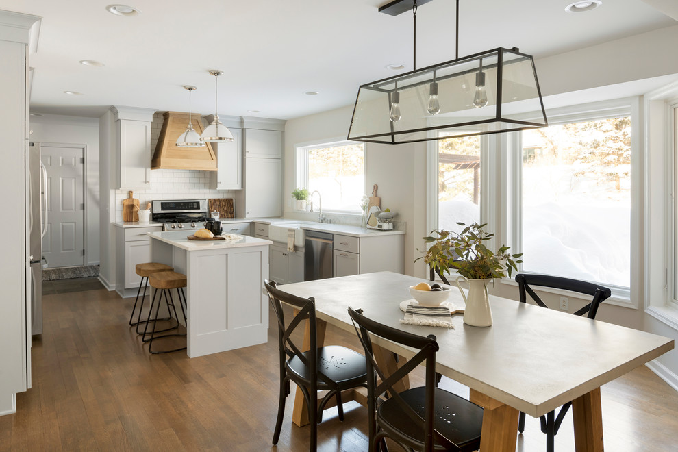 Bild på ett mellanstort lantligt vit vitt kök, med en rustik diskho, skåp i shakerstil, grå skåp, bänkskiva i kvarts, vitt stänkskydd, stänkskydd i tunnelbanekakel, rostfria vitvaror, mellanmörkt trägolv, en köksö och brunt golv