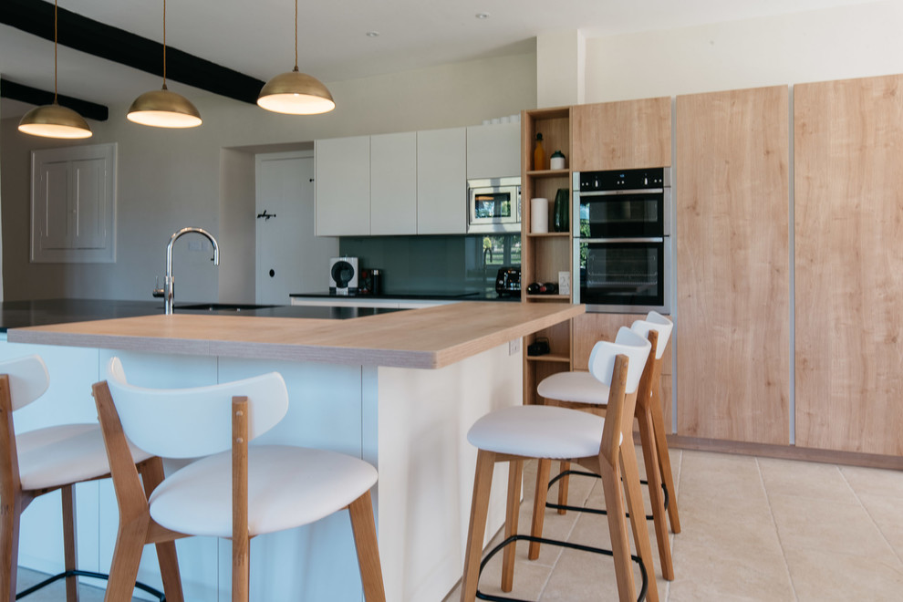 Cette photo montre une très grande cuisine américaine moderne avec un évier 2 bacs, un placard à porte plane, des portes de placard blanches, un plan de travail en granite, une crédence verte, une crédence en feuille de verre, un électroménager de couleur, un sol en carrelage de céramique, îlot, un sol beige et plan de travail noir.