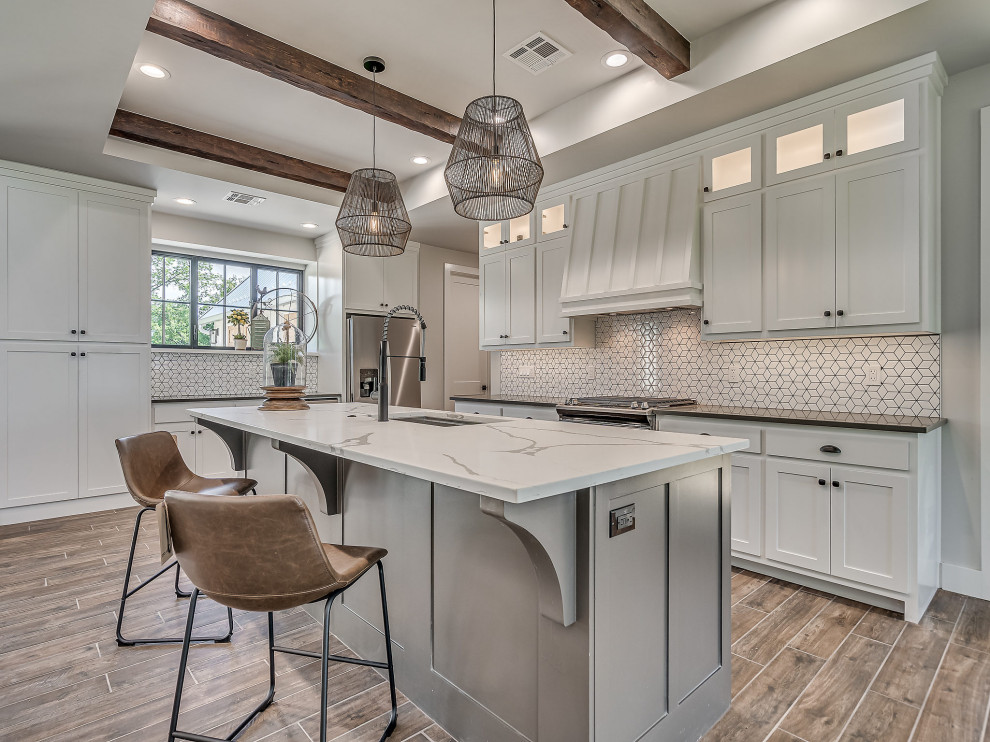 Example of a large cottage ceramic tile, brown floor and exposed beam eat-in kitchen design in Other with an undermount sink, shaker cabinets, white cabinets, quartz countertops, white backsplash, ceramic backsplash, stainless steel appliances, an island and white countertops