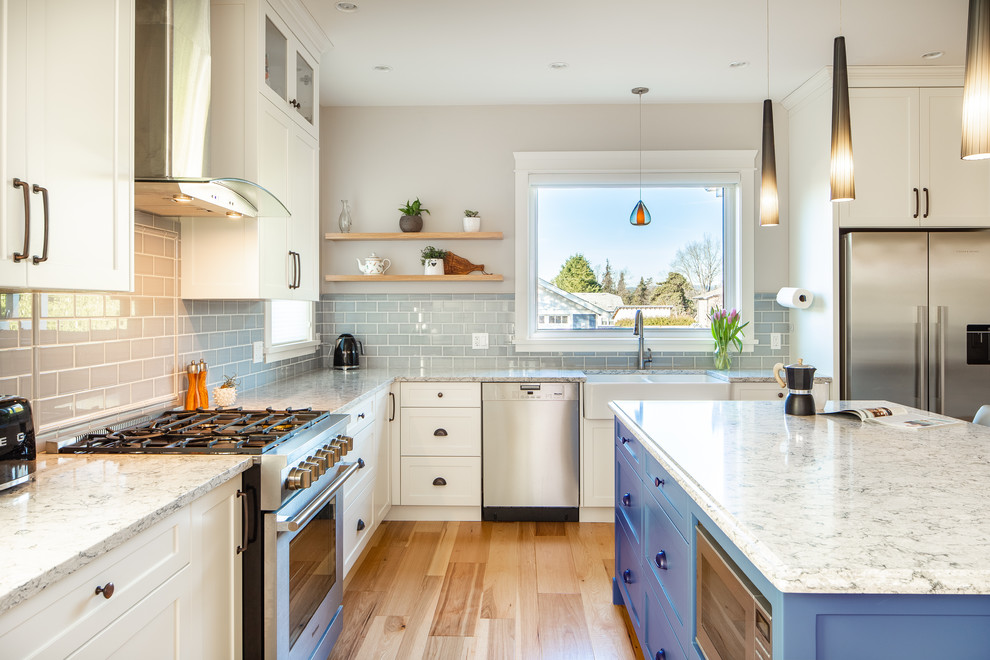 Inspiration for a large country l-shaped medium tone wood floor and brown floor eat-in kitchen remodel in Vancouver with a farmhouse sink, shaker cabinets, quartz countertops, gray backsplash, ceramic backsplash, stainless steel appliances, an island, white cabinets and gray countertops