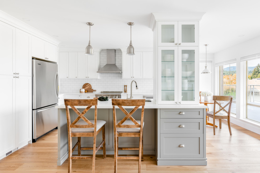 Example of a mid-sized cottage l-shaped medium tone wood floor and brown floor eat-in kitchen design in Vancouver with an undermount sink, shaker cabinets, gray cabinets, quartz countertops, white backsplash, subway tile backsplash, stainless steel appliances, an island and white countertops