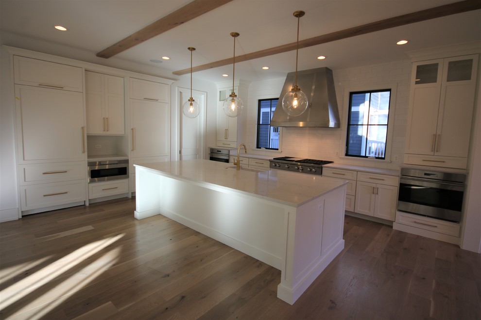 Large transitional l-shaped light wood floor and brown floor open concept kitchen photo in Chicago with a farmhouse sink, shaker cabinets, white cabinets, marble countertops, white backsplash, subway tile backsplash, stainless steel appliances, an island and white countertops