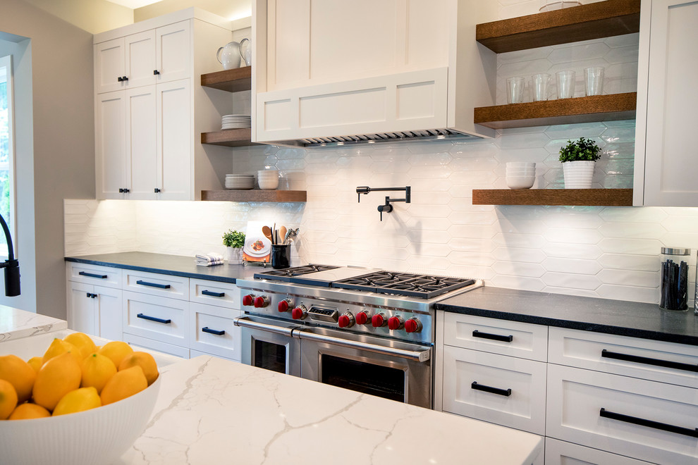 Design ideas for a farmhouse kitchen in Seattle with a belfast sink, shaker cabinets, white cabinets, engineered stone countertops, white splashback, porcelain splashback, stainless steel appliances, medium hardwood flooring, an island, brown floors and white worktops.