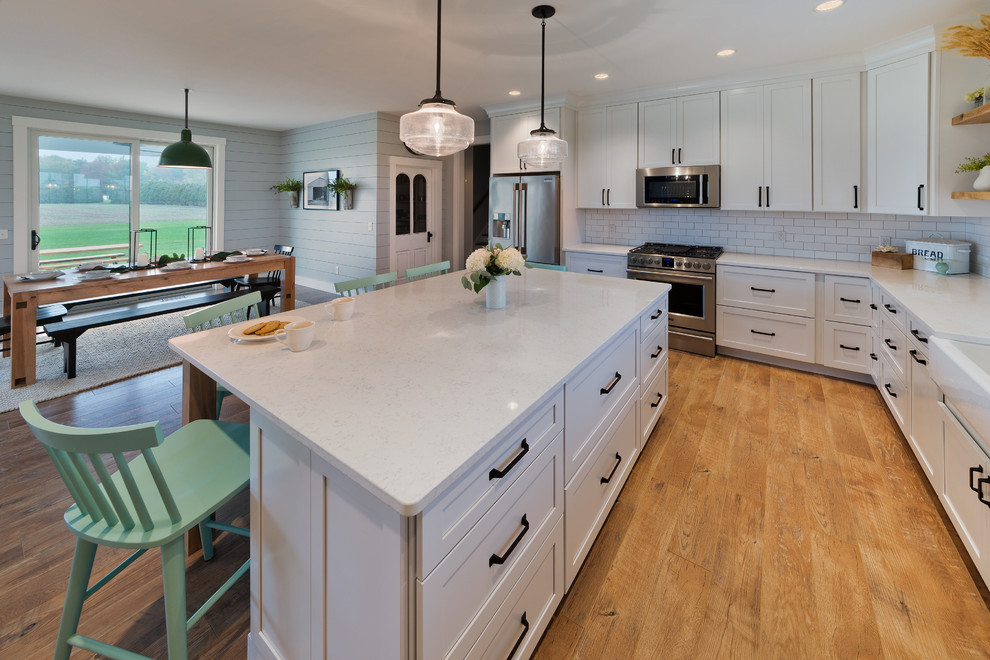 Eat-in kitchen - mid-sized farmhouse eat-in kitchen idea in Other with a farmhouse sink, white cabinets, marble countertops, white backsplash, subway tile backsplash, stainless steel appliances, an island and shaker cabinets