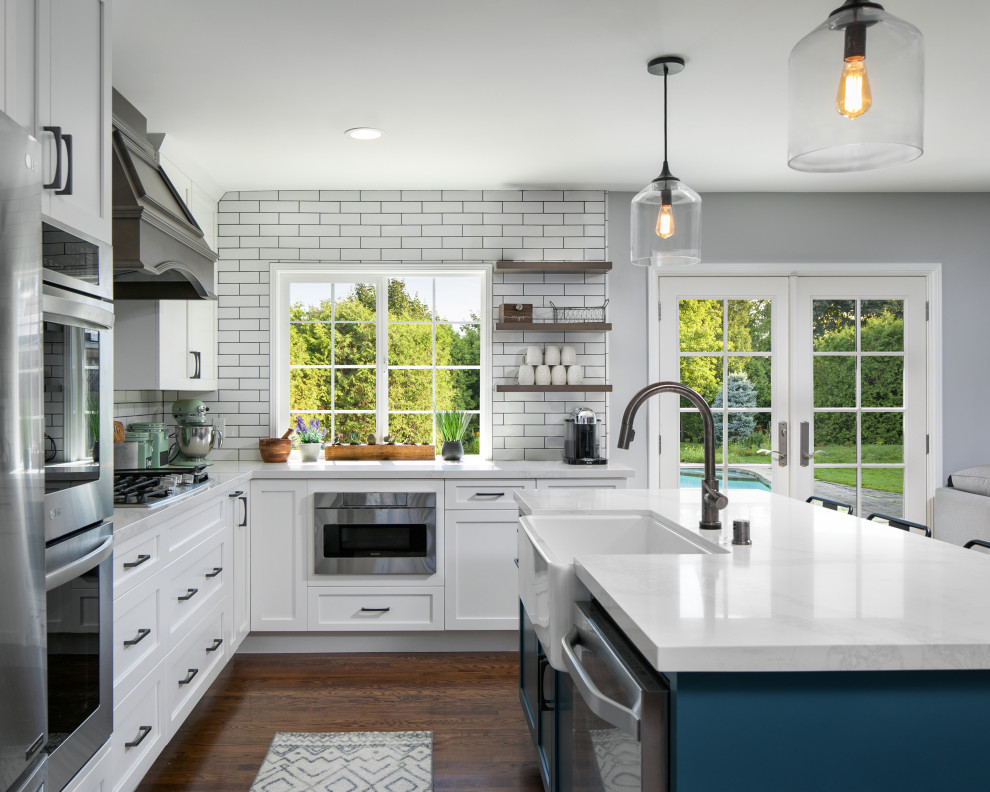 Mid-sized cottage l-shaped medium tone wood floor and brown floor eat-in kitchen photo in Los Angeles with a farmhouse sink, shaker cabinets, white cabinets, quartz countertops, white backsplash, porcelain backsplash, stainless steel appliances, an island and white countertops