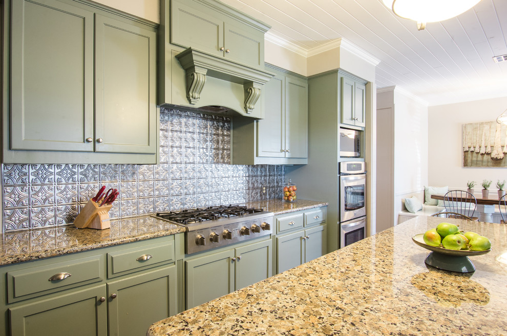 Foto på ett mellanstort lantligt kök, med en nedsänkt diskho, skåp i shakerstil, gröna skåp, granitbänkskiva, stänkskydd med metallisk yta, stänkskydd i metallkakel, rostfria vitvaror, mellanmörkt trägolv och en köksö