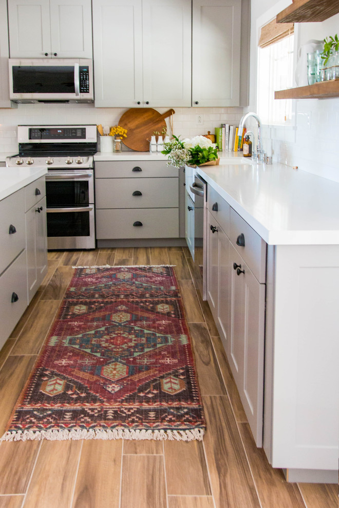 This is an example of a rural l-shaped open plan kitchen in Las Vegas with a belfast sink, shaker cabinets, grey cabinets, quartz worktops, white splashback, metro tiled splashback, stainless steel appliances, dark hardwood flooring, an island and beige floors.