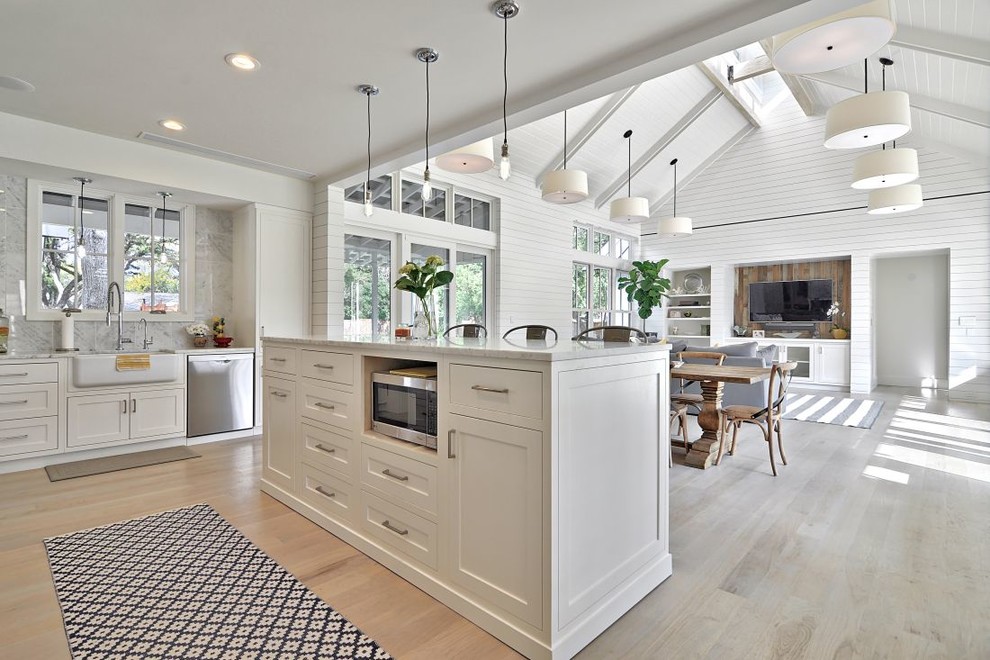 Inspiration for a country open plan kitchen in Austin with a belfast sink, shaker cabinets, white cabinets, marble worktops, white splashback, stone slab splashback, stainless steel appliances and light hardwood flooring.