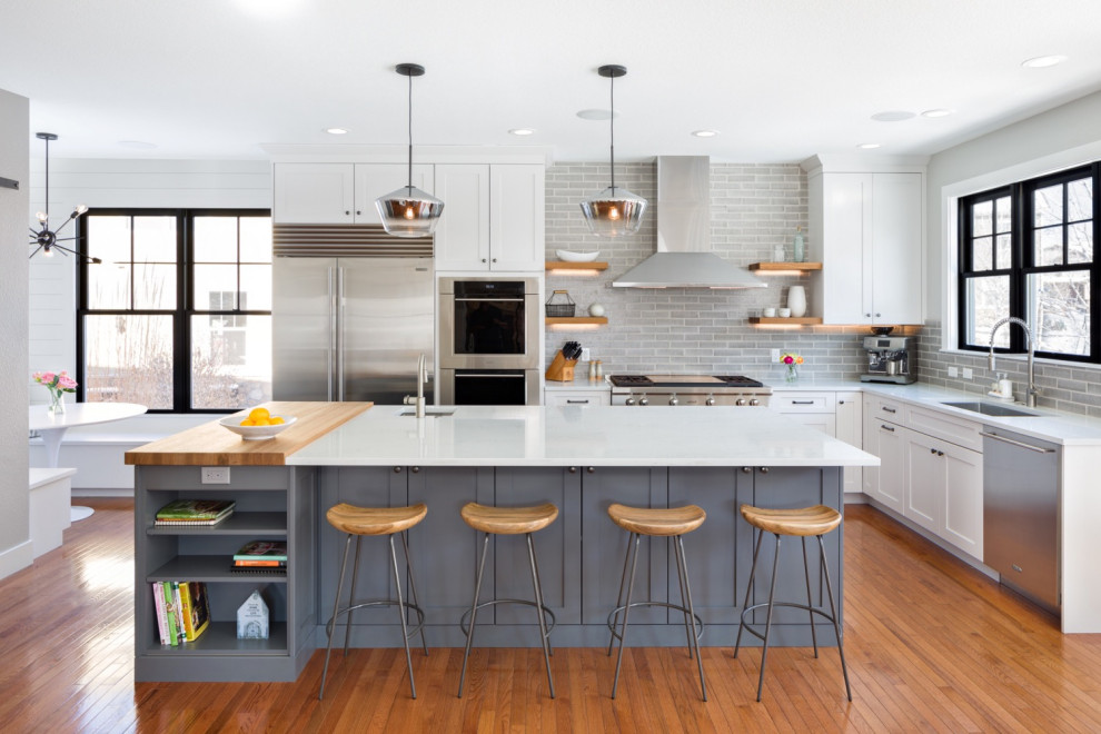 Photo of a large farmhouse l-shaped kitchen/diner in Denver with a submerged sink, recessed-panel cabinets, white cabinets, marble worktops, grey splashback, cement tile splashback, stainless steel appliances, dark hardwood flooring, an island, brown floors and white worktops.
