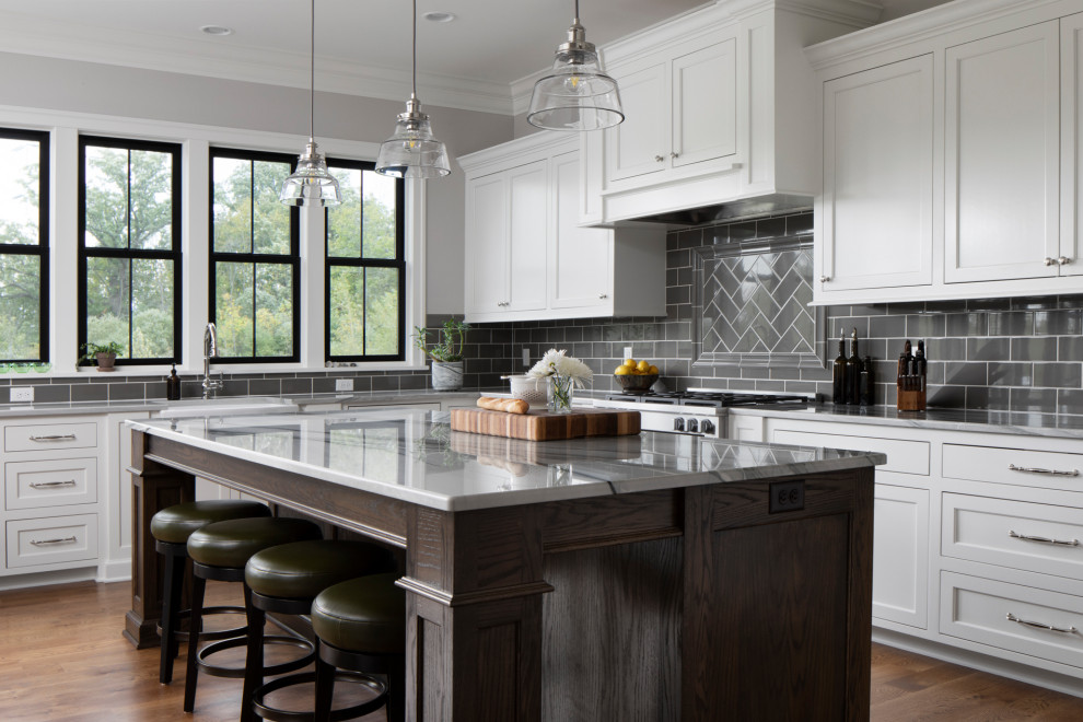 Inspiration for a large transitional u-shaped medium tone wood floor and brown floor eat-in kitchen remodel in Milwaukee with a farmhouse sink, shaker cabinets, white cabinets, gray backsplash, subway tile backsplash, an island, gray countertops and quartzite countertops