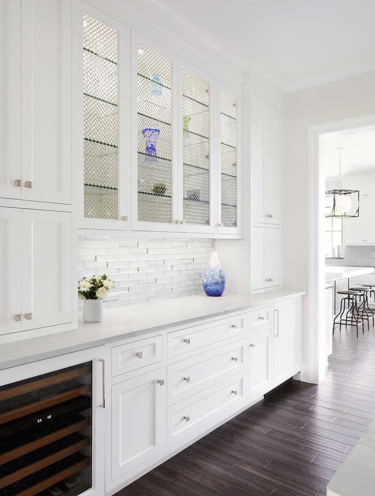 Medium sized traditional galley kitchen pantry in Chicago with glass-front cabinets, white cabinets, white splashback, glass tiled splashback, integrated appliances, dark hardwood flooring and brown floors.