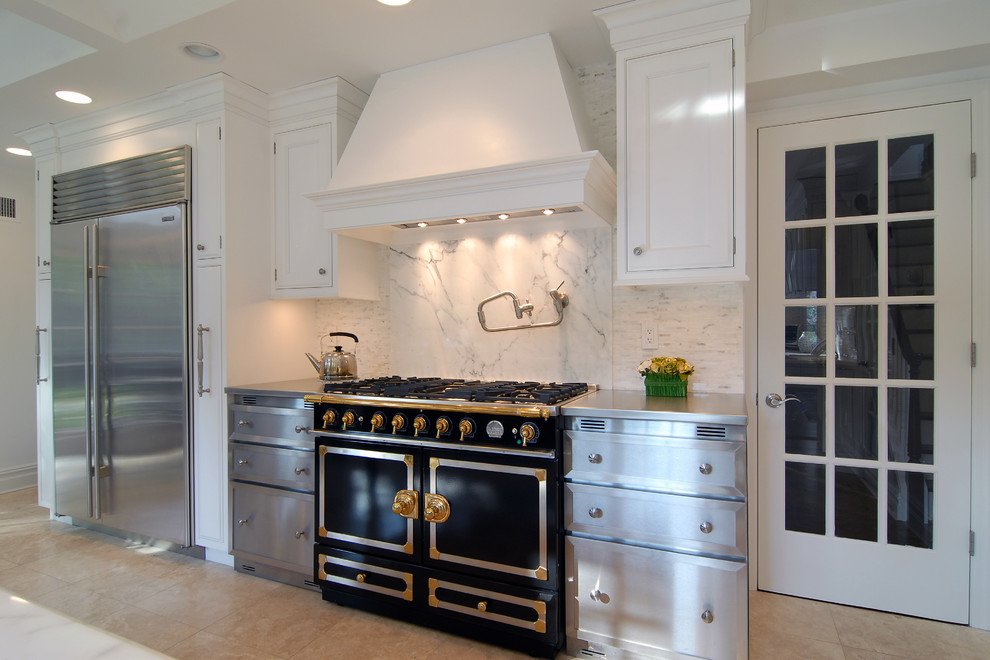 Mid-sized transitional l-shaped porcelain tile kitchen pantry photo in New York with a farmhouse sink, beaded inset cabinets, white cabinets, stainless steel countertops, multicolored backsplash, stone tile backsplash, stainless steel appliances and an island