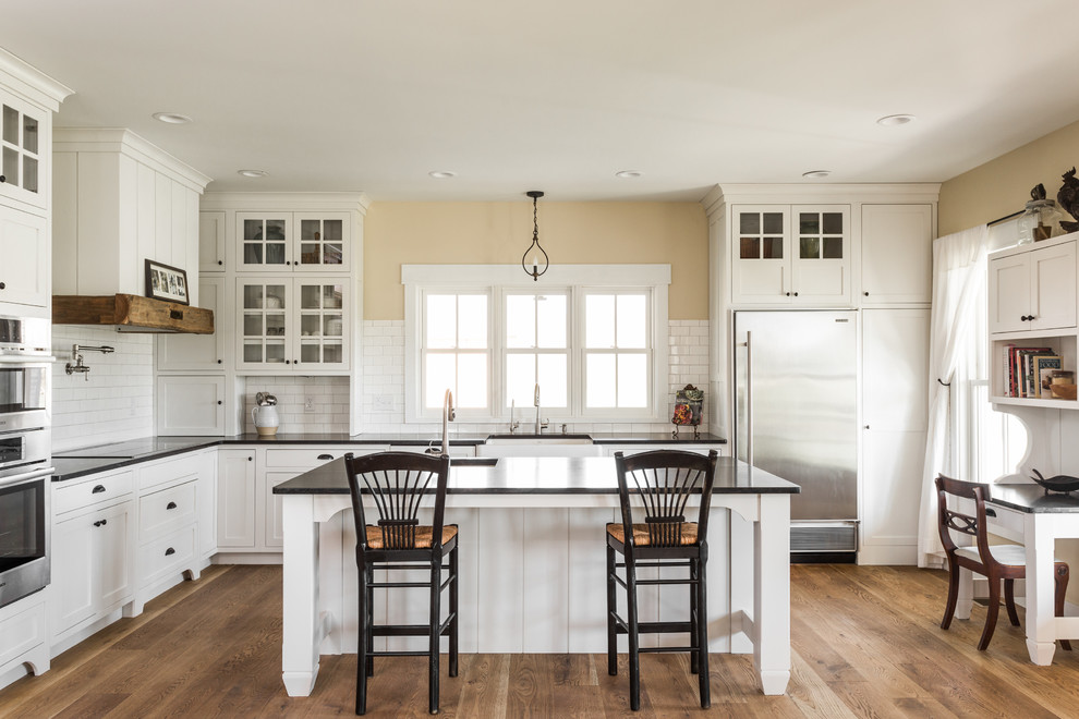 Foto de cocina de estilo de casa de campo grande con fregadero sobremueble, armarios estilo shaker, puertas de armario blancas, salpicadero blanco, salpicadero de azulejos tipo metro, electrodomésticos de acero inoxidable, suelo de madera en tonos medios y una isla