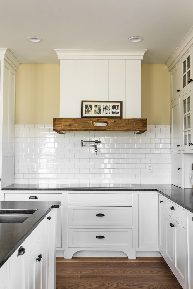 Inspiration for a large cottage u-shaped medium tone wood floor eat-in kitchen remodel in Indianapolis with a farmhouse sink, shaker cabinets, white cabinets, white backsplash, subway tile backsplash, stainless steel appliances and an island