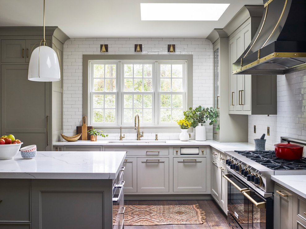 Foto på ett stort lantligt vit l-kök, med en dubbel diskho, bänkskiva i kvarts, vitt stänkskydd, stänkskydd i keramik, svarta vitvaror, mellanmörkt trägolv, en köksö, brunt golv, luckor med infälld panel och grå skåp