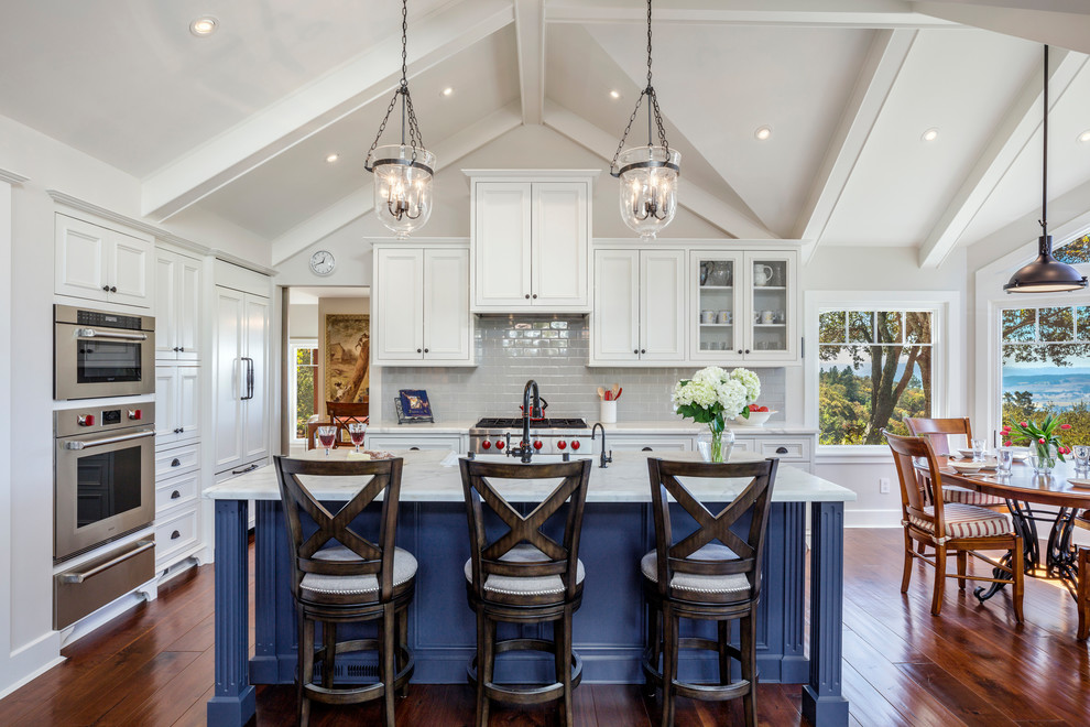 Open concept kitchen - mid-sized traditional l-shaped medium tone wood floor and brown floor open concept kitchen idea in Orange County with a farmhouse sink, blue cabinets, marble countertops, ceramic backsplash, stainless steel appliances, an island, beaded inset cabinets and gray backsplash