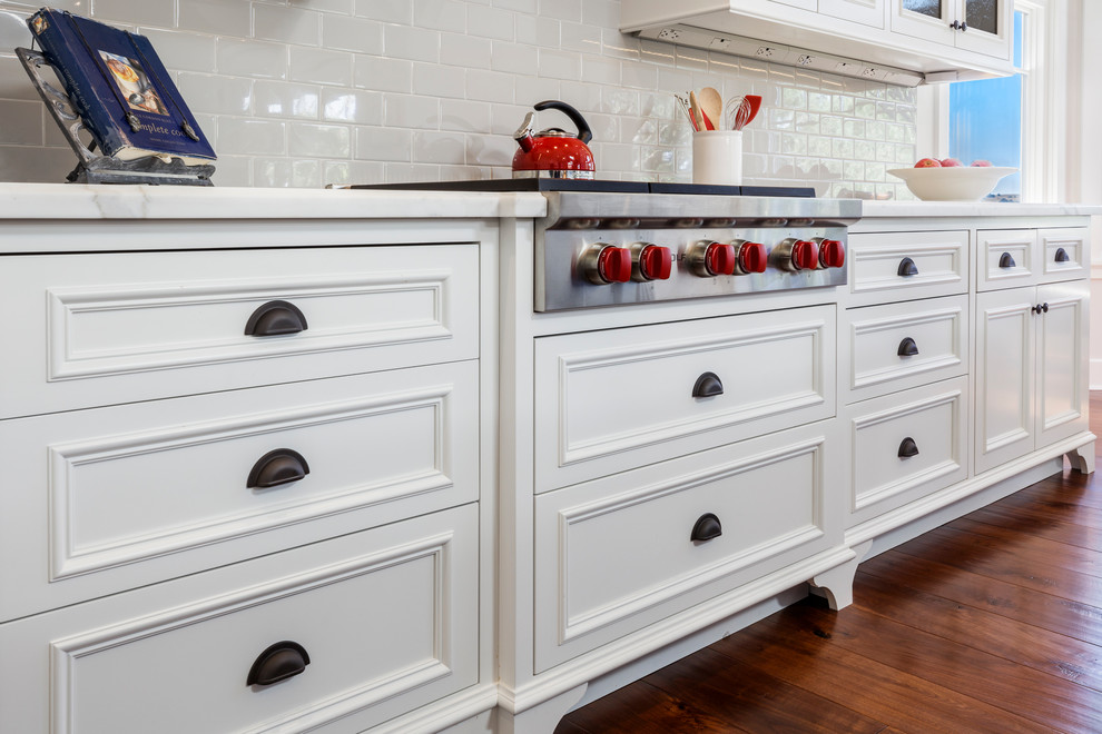 Klassisk inredning av ett mellanstort kök, med en rustik diskho, vita skåp, marmorbänkskiva, stänkskydd i keramik, rostfria vitvaror, mellanmörkt trägolv, en köksö, brunt golv, luckor med profilerade fronter och grått stänkskydd