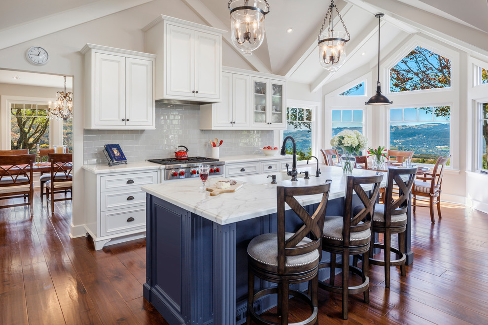 Inspiration for a mid-sized timeless l-shaped brown floor and dark wood floor open concept kitchen remodel in Orange County with a farmhouse sink, marble countertops, ceramic backsplash, stainless steel appliances, an island, beaded inset cabinets, gray backsplash and white cabinets