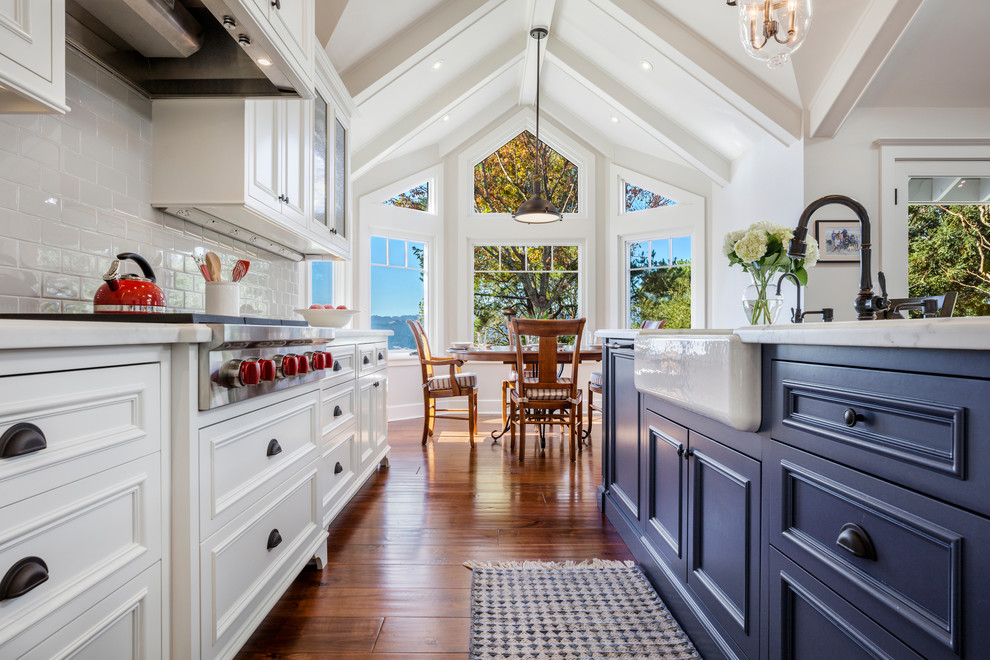 Klassisk inredning av ett mellanstort kök, med en rustik diskho, blå skåp, marmorbänkskiva, stänkskydd i keramik, rostfria vitvaror, mellanmörkt trägolv, en köksö, brunt golv, luckor med profilerade fronter och grått stänkskydd