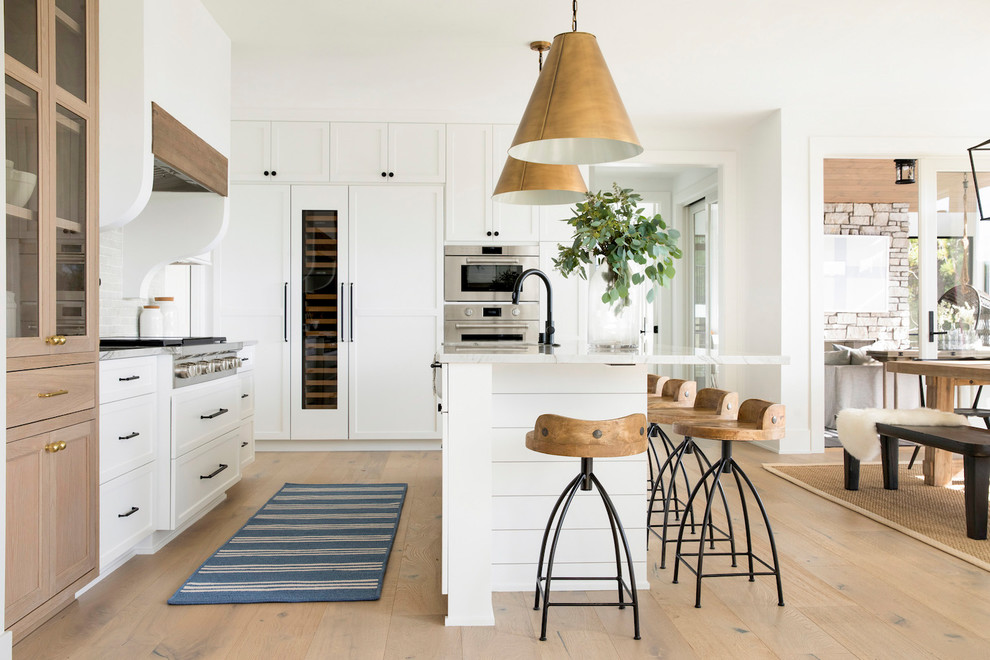 This is an example of a farmhouse kitchen/diner in Minneapolis with shaker cabinets, white cabinets, integrated appliances, light hardwood flooring, an island and grey worktops.