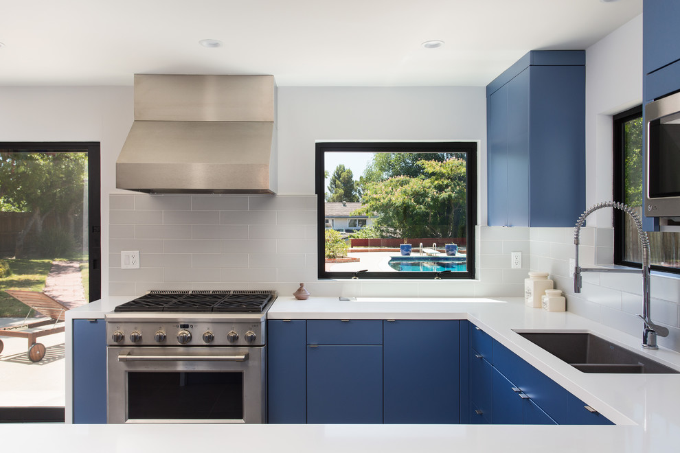 Photo of a small modern u-shaped kitchen/diner in Los Angeles with a submerged sink, flat-panel cabinets, blue cabinets, engineered stone countertops, grey splashback, metro tiled splashback, stainless steel appliances, porcelain flooring, no island, grey floors and white worktops.