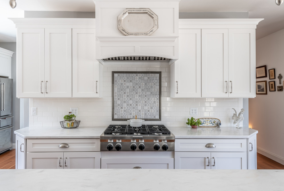Example of a large classic u-shaped medium tone wood floor open concept kitchen design in Other with an undermount sink, recessed-panel cabinets, white cabinets, solid surface countertops, multicolored backsplash, ceramic backsplash, stainless steel appliances, an island and white countertops