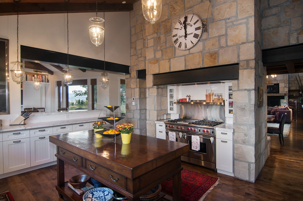 Rustik inredning av ett kök, med skåp i shakerstil, vita skåp, träbänkskiva, en köksö, stänkskydd med metallisk yta, rostfria vitvaror och mörkt trägolv