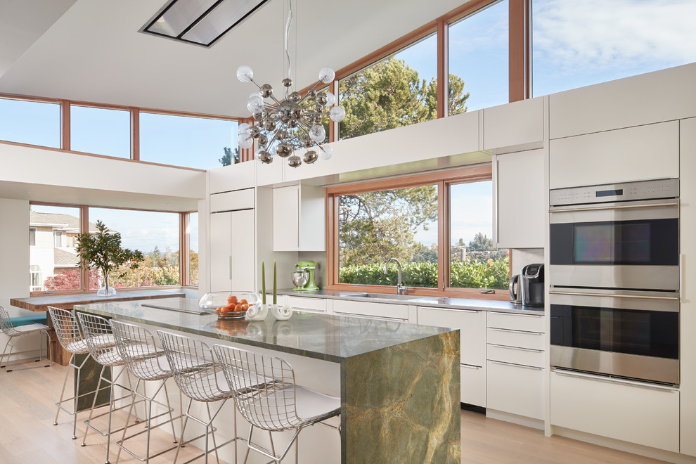 Moderne Wohnküche in L-Form mit flächenbündigen Schrankfronten, weißen Schränken, Rückwand-Fenster, Küchengeräten aus Edelstahl, braunem Holzboden, Kücheninsel, braunem Boden und grüner Arbeitsplatte in Seattle