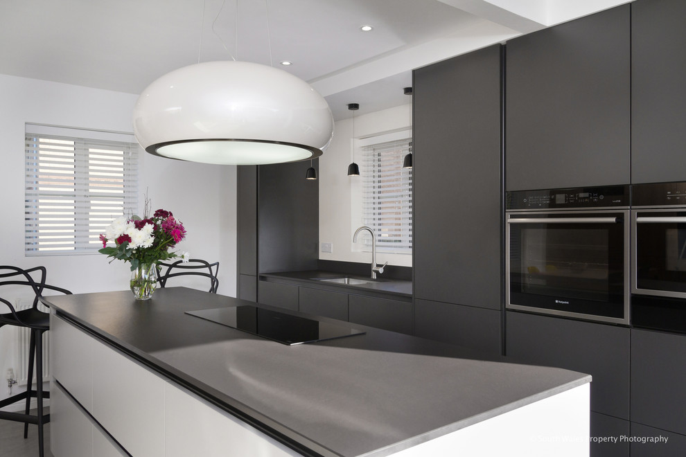 This is an example of a small contemporary grey and cream single-wall kitchen/diner in Other with flat-panel cabinets, black cabinets, composite countertops, black appliances, ceramic flooring, an island, grey floors and black worktops.