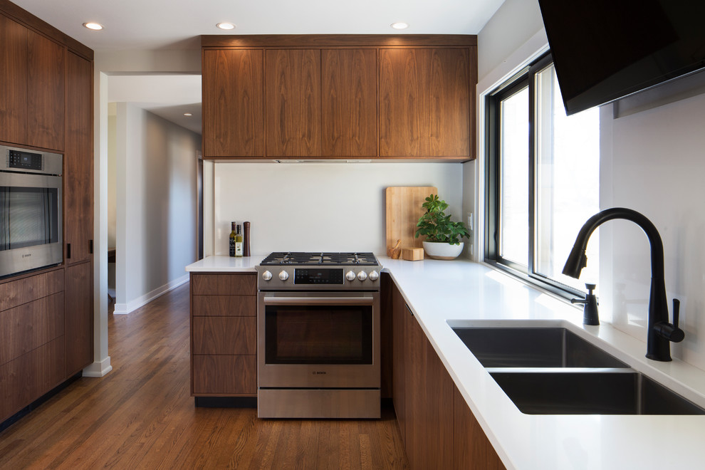 Example of a mid-sized minimalist u-shaped medium tone wood floor and red floor enclosed kitchen design in Milwaukee with an undermount sink, flat-panel cabinets, brown cabinets, quartz countertops, white backsplash, stone slab backsplash, stainless steel appliances and no island
