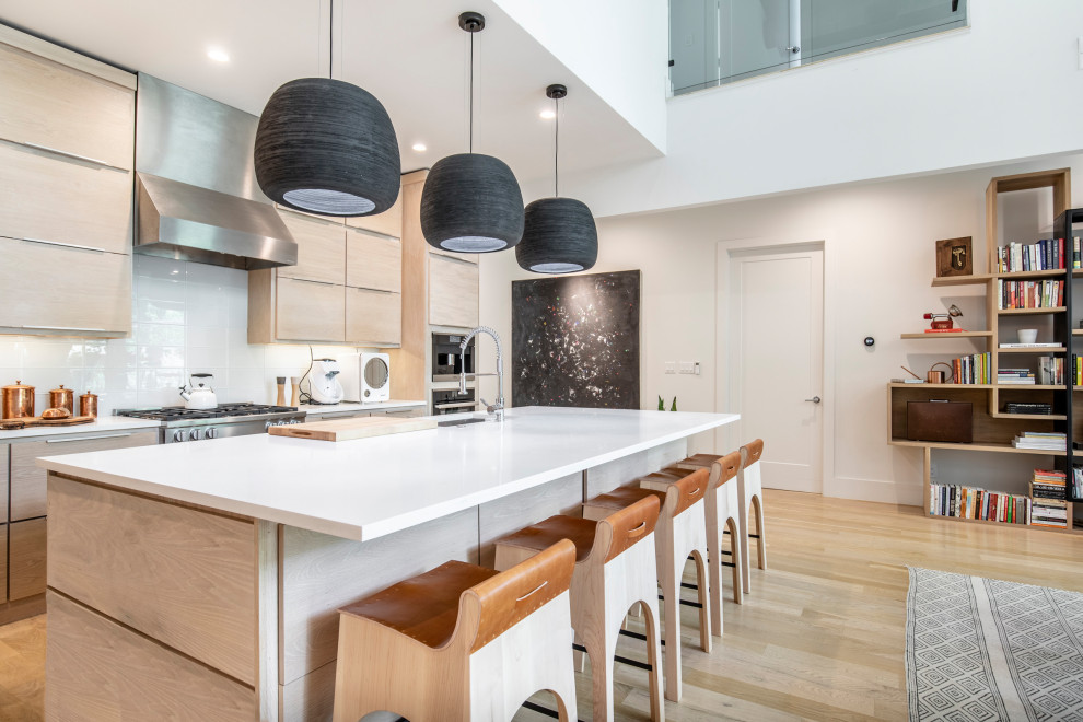 Example of a trendy galley light wood floor and beige floor open concept kitchen design in Dallas with an undermount sink, flat-panel cabinets, light wood cabinets, white backsplash, stainless steel appliances, an island and white countertops