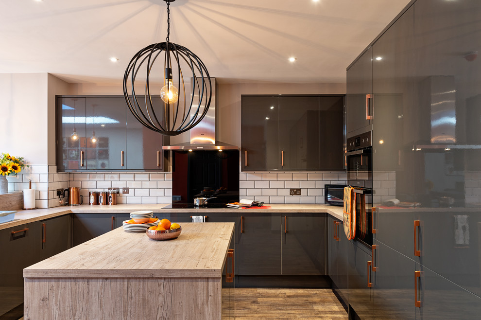Large trendy u-shaped medium tone wood floor and beige floor open concept kitchen photo in Oxfordshire with an island, flat-panel cabinets, gray cabinets, wood countertops, white backsplash, subway tile backsplash, stainless steel appliances and beige countertops