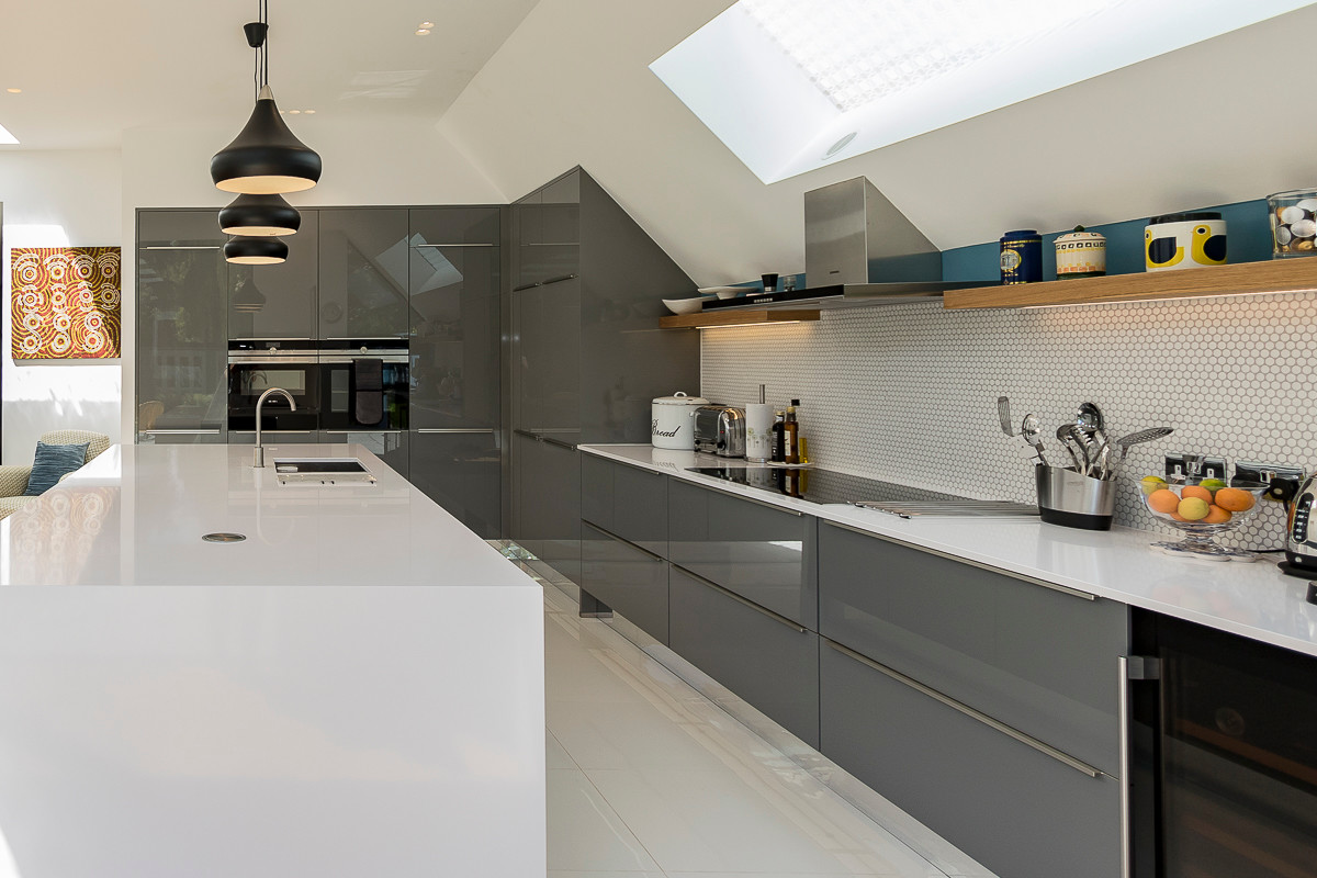 Design ideas for a large contemporary single-wall kitchen in London with grey cabinets, an island, a submerged sink, flat-panel cabinets, white splashback, integrated appliances, light hardwood flooring and brown floors.