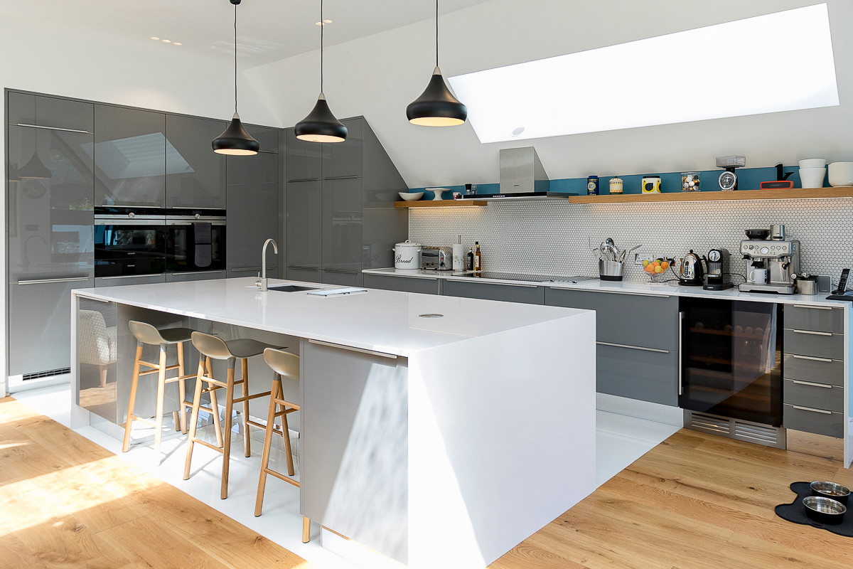 This is an example of a large contemporary single-wall kitchen in London with grey cabinets, an island, a submerged sink, flat-panel cabinets, white splashback, integrated appliances, light hardwood flooring and brown floors.